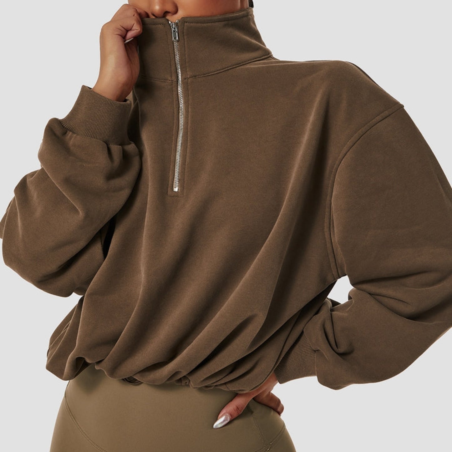 FITNESS MODEL WEARING A CHOCOLATE BROWN, CROPPED, PAPER BAG SWEAT SHIRT  WITH FRONT NECK ZIPPER OPENING FROM VIBRAS ACTIVEWEAR.