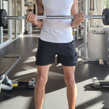 young male doing bicep curls with the bar at the gym while wearing a pair of black elijah gym shorts from vibras activewear