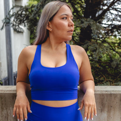 Fitness model wearing a beautiful, blue and high impact sports bra posing in nature